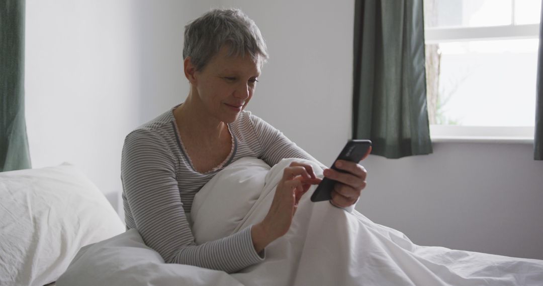 Senior Woman Using Smartphone in Bed Next to Window - Free Images, Stock Photos and Pictures on Pikwizard.com