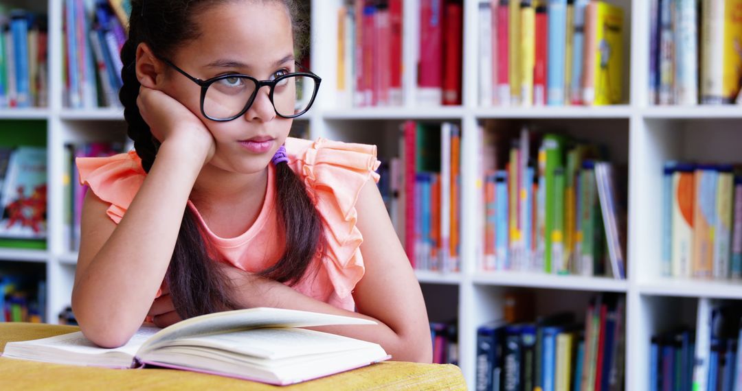 Thoughtful Girl with Glasses Sitting in Library with Open Book - Free Images, Stock Photos and Pictures on Pikwizard.com