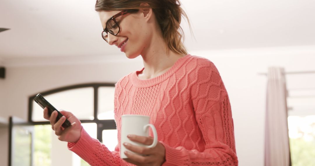 Smiling woman in pink sweater using smartphone and holding coffee - Free Images, Stock Photos and Pictures on Pikwizard.com