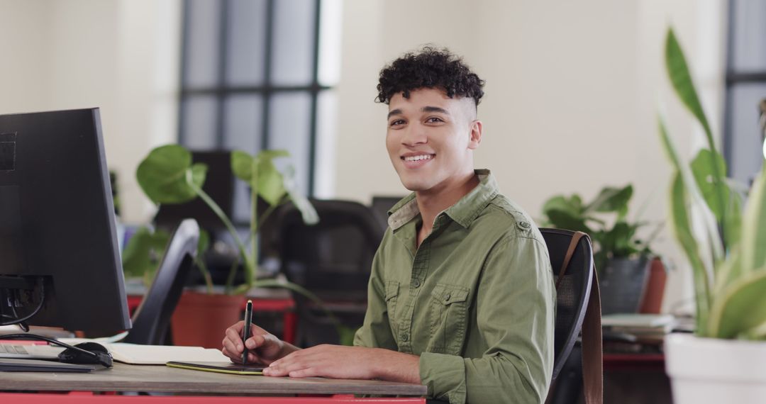 Young Man Smiling at Desk in Modern Office with Green Plants - Free Images, Stock Photos and Pictures on Pikwizard.com