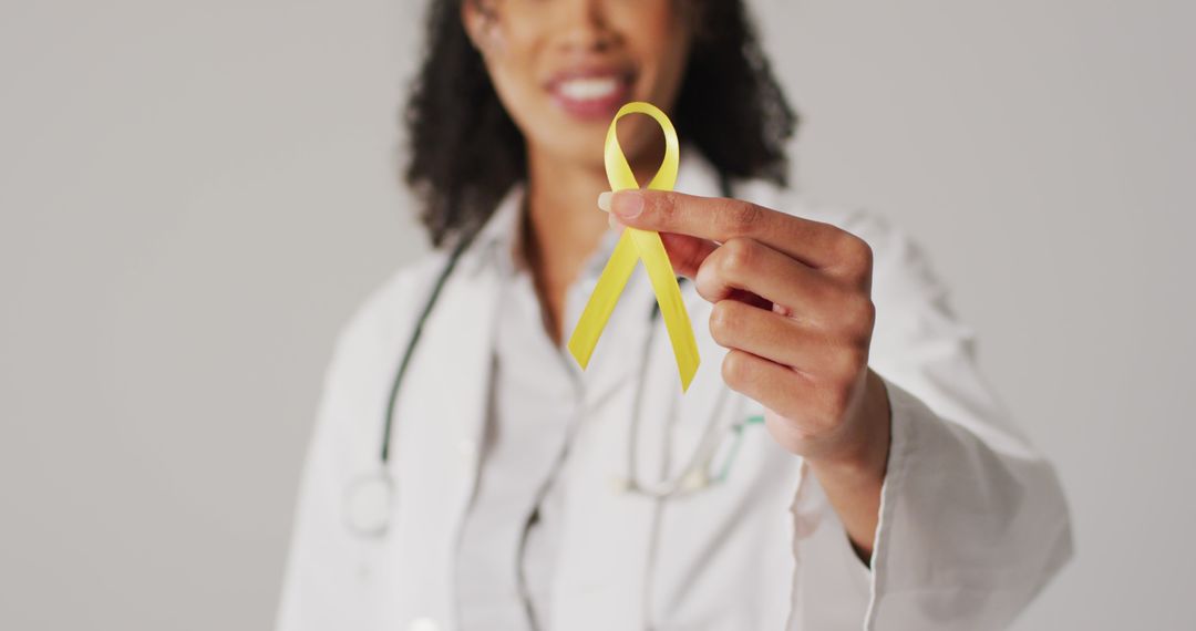 Image of smiling biracial female doctor holding yellow bladder cancer ribbon - Free Images, Stock Photos and Pictures on Pikwizard.com
