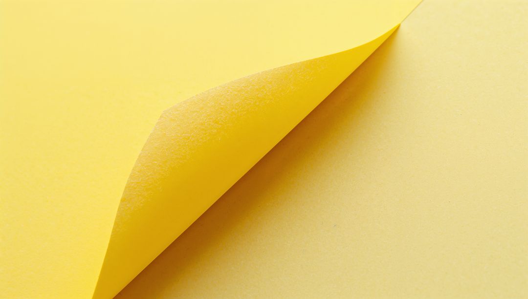 Yellow paper sheet curling upper-right corner revealing textured underside, minimal background