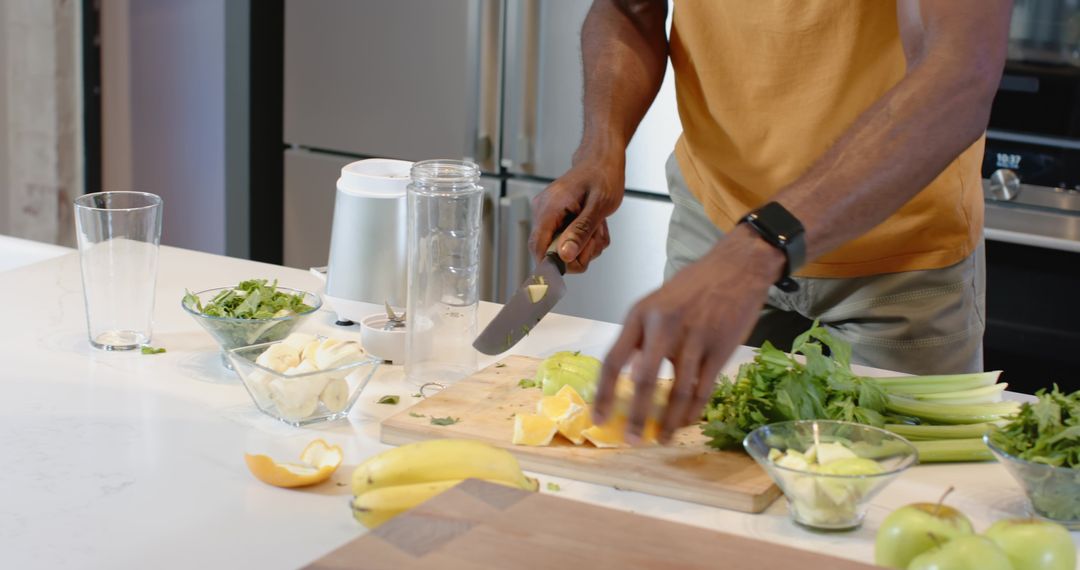 Man chopping citrus and greens on kitchen island preparing smoothie, wearing mustard tee
