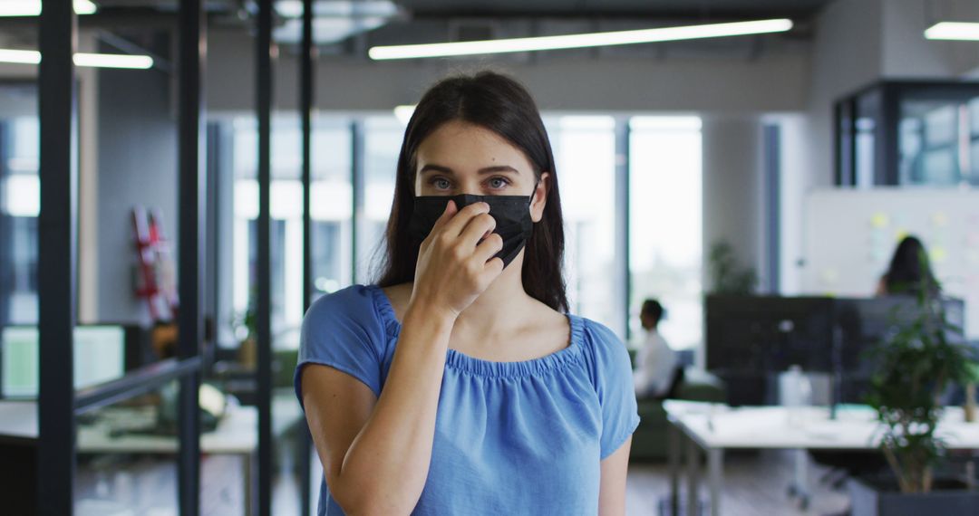 Young Woman in Modern Office Adjusting Her Face Mask - Free Images, Stock Photos and Pictures on Pikwizard.com