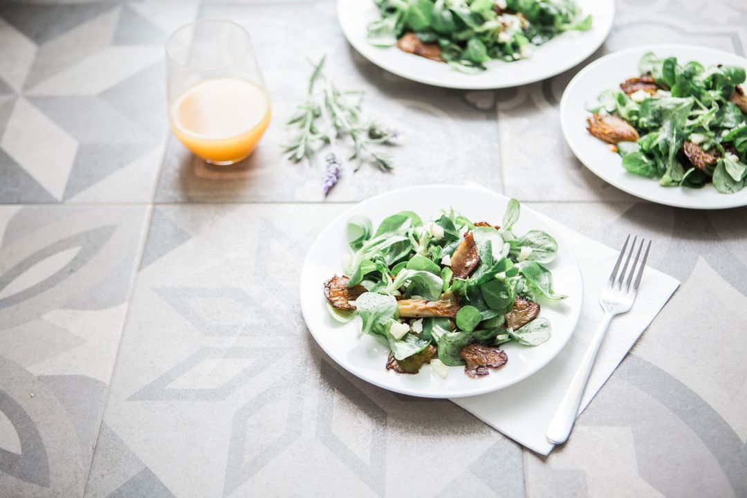 Fresh green salad featuring roasted mushrooms, citrus juice and herb garnish on patterned tile