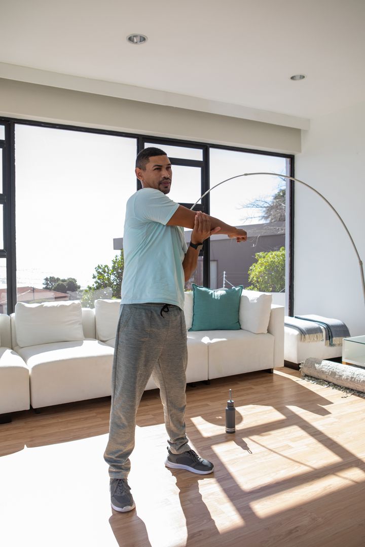 Man Stretching at Home for Fitness Routine in Sunlit Living Room