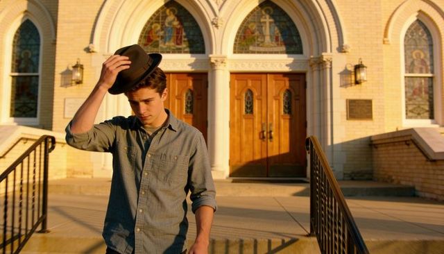 Teen tipping fedora while descending vintage church steps at golden hour with wooden doors