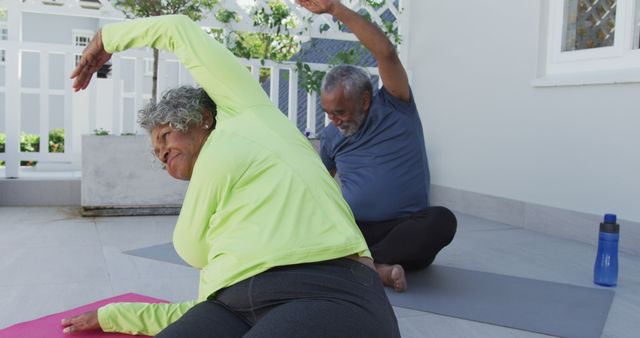 Happy african american senior couple practicing yoga on mat on patio. active and healthy retirement lifestyle at home and garden.
