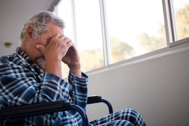 Side view of sad senior man sitting on wheelchair in nursing home