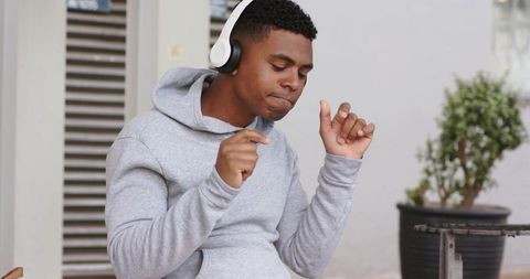 African american man listening to music with wireless headphones on porch in gray hoodie