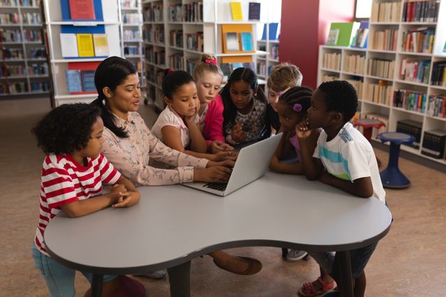 This image shows a female teacher engaging a group of diverse elementary school students with a laptop in a school library. Ideal for educational content, school brochures, technology in education articles, and multicultural learning resources.
