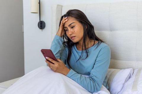 Pensive asian woman checking phone in bed experiencing worry and late night scrolling