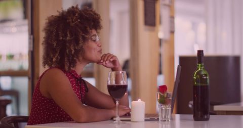 Woman Savoring Wine While Engaged in Laptop Video Call Indoors
