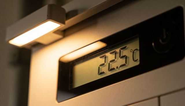 Digital thermostat display showing 22.5°c on brushed metal panel with task lamp and power button