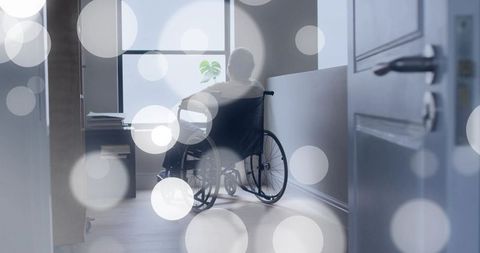 Senior man in wheelchair gazing out frosted window in quiet corridor with plant and books