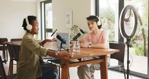 Diverse duo recording conversational podcast at home studio with ring light and studio microphones
