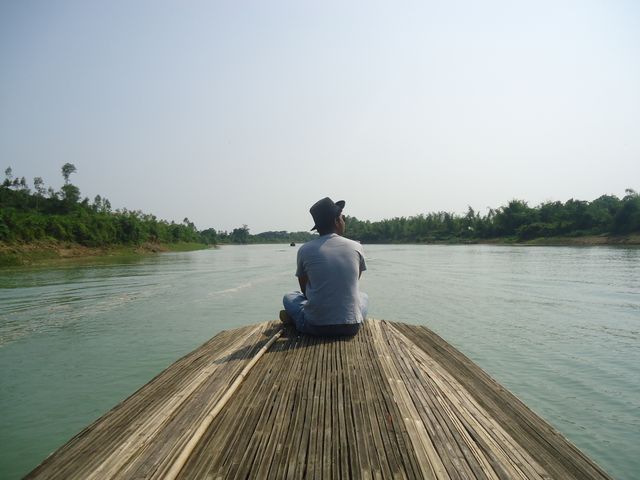 Man sitting on back of boat, quietly enjoying calm river journey. Useful for travel blogs, adventure magazines, tourism promotions, and nature-focused advertising. Conveys peace, adventure, and exploration.