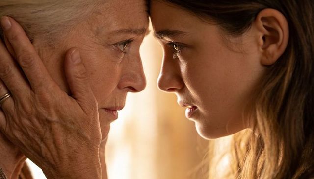 Senior woman holding teen's face in tender forehead embrace with warm backlight