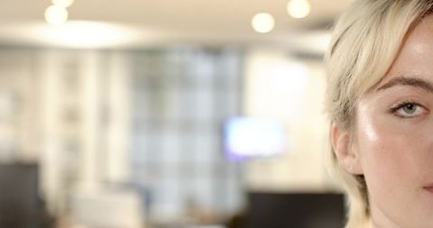 Half-face portrait of blonde woman in modern office bokeh closeup with calm expression