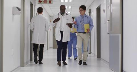 Medical Team Walking and Checking Tablet While Discussing Patient Care in Hospital Corridor