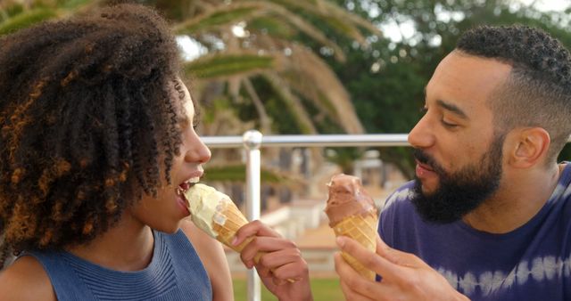 Romantic diverse couple siting by railing, smiling and eating ice creams. Summer, vacation, romance, love, relationship, free time and lifestyle, unaltered.