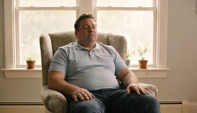 Middle-aged man relaxing in armchair by sunlit sash windows with houseplants
