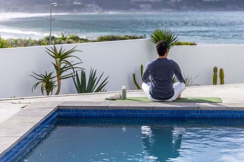 Man Meditating on Yoga Mat by Pool with Ocean View Coastal Terrace Morning Wellness