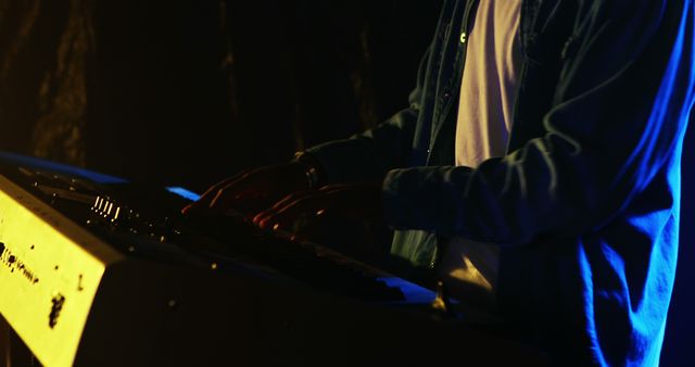 Musician playing keyboard on stage during a live performance, captured with dramatic, moody lighting. This dynamic image captures the emotions and dedication of a live musical artist. Ideal for use in articles or promotions about live music, concerts, musician profiles, or as a background for music websites and blogs.