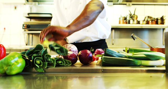 This image shows a chef engaged in preparing fresh vegetables in a professional kitchen, highlighting culinary skills and food preparation. Ideal for use in content about cooking classes, restaurant promotions, culinary schools, or healthy eating.