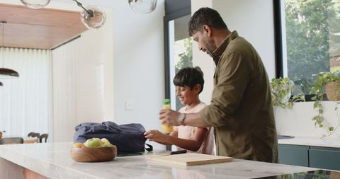 Father and son packing backpack in modern kitchen