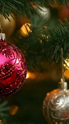 Vertical holiday video showing swaying red-pink and silver baubles with warm bokeh lights