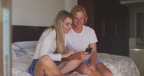 Joyful Couple Enjoying Smartphone Leisure in Bedroom