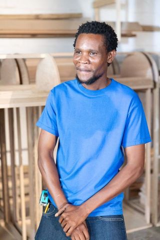 African american carpenter measuring wooden furniture frames in bright workshop
