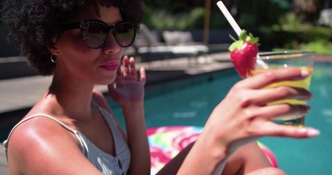 African american woman relaxing on pool float with cocktail and sunglasses