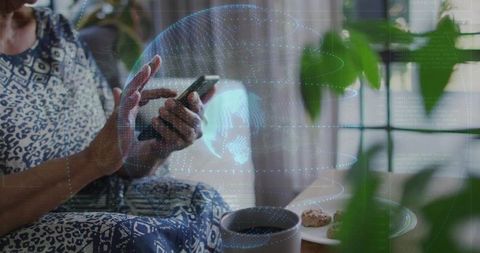 Senior woman using smartphone at home with augmented reality globe overlay, cozy scene