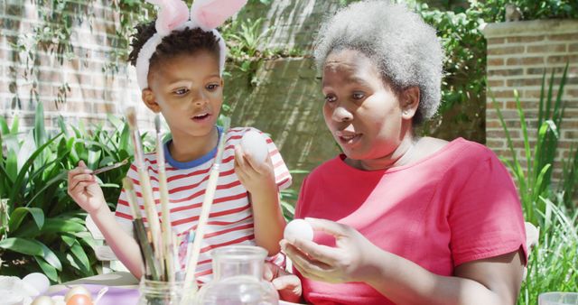 Happy african american grandmother and grandson decorating easter eggs in sunny garden, slow motion - Download Free Stock Photos Pikwizard.com