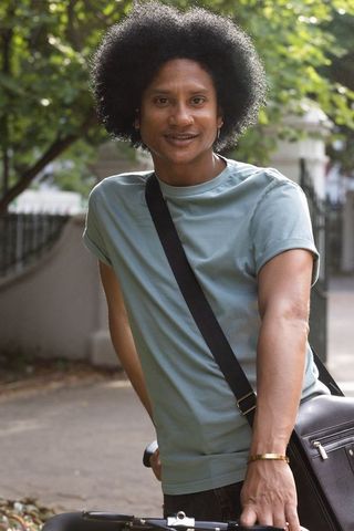 African american man standing with bicycle on tree-lined sidewalk carrying crossbody bag