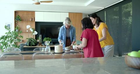 Three women setting table for casual home gathering in modern open-plan living room