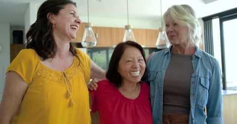 Laughing friends sharing warm moment in modern kitchen, diverse women smiling together