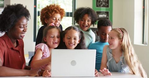 Smiling teacher guiding diverse students around laptop for collaborative learning
