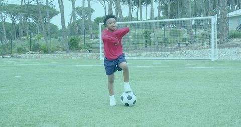 Young boy balancing on soccer ball on outdoor pitch practicing ball control and confidence