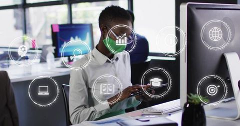 Masked office worker using tablet with floating digital business icons in modern workspace