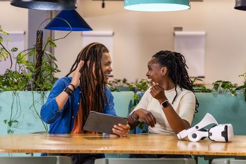 African American coworkers laughing and collaborating with tablet and VR headset in coworking lounge