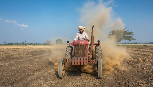 Farmer driving red tractor on dusty farmland
