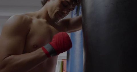 Determined Shirtless Boxer Leaning on Punching Bag in Gym