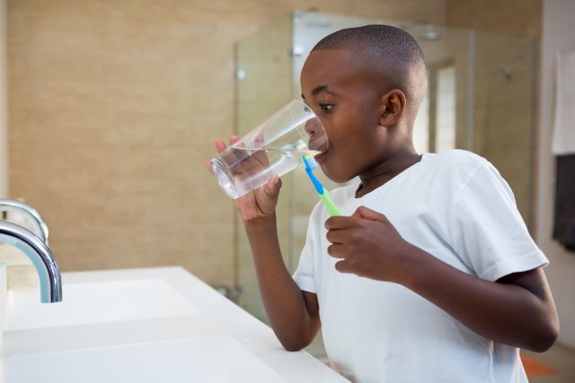 Boy drinking water from glass while standing by sink