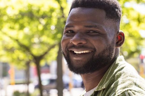 Smiling african man enjoying sunny urban day wearing green shirt close-up headshot