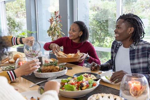 African american friends sharing homemade meal and passing bread at sunny dining table
