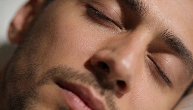 Closeup male face resting with closed eyes and light stubble showing skin texture, serene