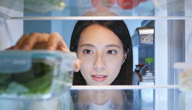 Young woman reaching for leafy greens in refrigerator during healthy meal prep